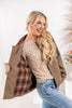 A woman modeling a tan corduroy-like button-up jacket with a brown and black plaid lining, worn open over a beige polka-dot top and blue jeans.