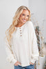 A woman wearing a cream waffle knit long-sleeve henley top with brown buttons, paired with blue jeans.