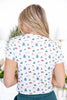 A woman viewed from behind wearing a white short-sleeve top with a colorful Christmas-themed print of snowmen, trees, and sleighs.