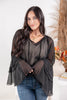 A woman wearing a black long-sleeve blouse with a V-neck and tiered bell sleeve flared cuffs.