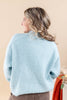 A woman shown from the back wearing a light blue ribbed knit sweater, set against a solid beige background.