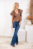 A woman models a brown ruffled peplum top with blue flare jeans.