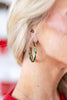 A close-up of a woman's ear wearing a small twisted candy cane earring with green and red enamel-like stripes.