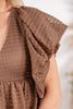 Close-up of a woman wearing a brown textured sleeveless top a draped ruffle detail on the shoulder.
