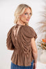 A woman wearing a brown textured short-sleeve top with puff sleeves and a tie-back neckline.