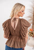 A woman shown from the back wearing a brown smocked peplum top with dramatic puffed cap sleeves and a tie neckline.