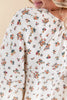Close-up of a woman wearing a cream-colored blouse with a dense small floral print in orange, red, yellow, and green.