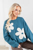 A woman wearing a teal blue sweatshirt with large white flower appliqués.
