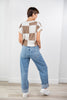 A woman is shown from behind wearing a brown and white checkered short-sleeve knit top and jeans.
