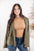 A woman modeling an olive green utility jacket with brown collar, worn over a tan top and blue jeans.
