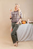 A woman modeling a brown and beige plaid short-sleeve top with olive green pants, holding a martini glass in front of a styled table with candles and a pumpkin.