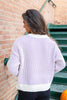 A woman wearing a white knit sweater with purple vertical stripes in an outdoor setting