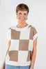 A woman wearing a short-sleeve knit sweater with a beige and off-white checkered pattern.