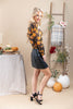 A woman models a long-sleeve black blouse with a yellow and orange floral pattern, paired with a black faux-leather mini skirt and black strappy heels, in a styled autumn-themed studio setting.