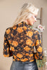 A woman shown from the back wearing a sheer black long-sleeve blouse with a large orange and yellow floral print, paired with dark gray leather pants.