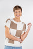 A woman wearing a short-sleeve knit sweater with a beige and off-white checkered pattern.