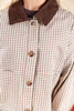 Close-up of a woman wearing a buttoned white and beige gingham jacket with a dark brown corduroy collar and brown buttons.