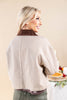 A woman shown from the back wearing a cropped brown and beige gingham jacket with a dark brown corduroy collar, set against a warm beige background.