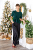 A woman stands wearing a dark green short-sleeve knit top and black wide-leg pants with lace trim at the hem.