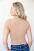 A woman with blonde hair is shown from the back wearing a beige short-sleeve textured knit top and blue jeans against a plain white background.