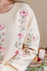 Close-up of a cream-colored knit sweater with pink floral embroidery and green stems, worn by a model.