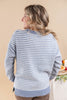 A woman shown from the back wearing a light blue and white houndstooth scallop pattern knit sweater, set against a warm beige background.