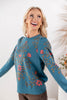 A woman wearing a teal long-sleeve knit sweater with pink floral and gold vine embroidery.