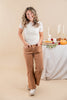 A woman modeling a white short-sleeve t-shirt with a small yellow floral pattern and brown wide-leg jeans, standing in front of a beige studio backdrop with a decorated autumn table in the background.