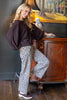 A woman posing in a room next to a wooden cabinet, wearing a dark brown bubble-sleeve top and leopard-print wide-leg pants.