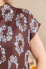 Close-up of a person wearing a brown short-sleeve top with a light blue and white floral pattern, showing the shoulder and upper arm against a soft beige background.