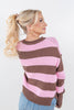 A woman with blonde hair in a ponytail is shown from the back wearing a pink and brown striped knit sweater and blue jeans against a plain white background.