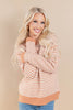 A smiling blonde woman wearing a peach and cream houndstooth knit sweater with a solid peach ribbed collar, cuffs, and hem, paired with blue jeans, set against a solid beige studio background.
