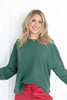 A woman wearing a dark green ribbed knit long-sleeve top and red drawstring pants.
