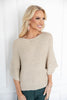 A woman wearing a beige textured knit sweater with elbow-length sleeves and dark green pants.