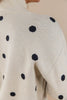Close-up of a knit sweater with a cream base and black polka dots, worn by a woman.