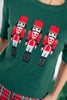 A close-up of a dark green knit sweater featuring three embroidered nutcracker figures across the chest.