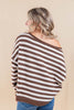 A woman shown from the back wearing an off-the-shoulder brown and white striped knit sweater, paired with blue jeans, against a solid beige studio background.