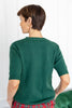 A woman shown from the back wearing a dark green short-sleeve knit sweater and red plaid pants.