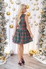 A woman stands wearing a sleeveless green plaid mini dress with red and white stripes, paired with burgundy high heels.