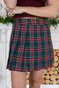 A woman wearing a dark green pleated plaid mini skirt with red, white, and yellow stripes, paired with a dark red top.