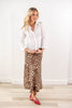 A woman modeling a white long-sleeve button-up shirt and a brown leopard-print midi skirt, paired with red pointed flats, standing against a white wall and light wood floor.