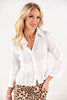 A blonde woman wearing a white long-sleeve button-up shirt with a subtle vertical stripe texture and a gathered waist, paired with a leopard print skirt, against a plain white studio background.