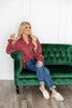 A woman sits on a green sofa, wearing a red and black plaid button-down shirt, blue jeans, and beige slip-on shoes.