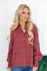 A woman wearing a red and green plaid button-up shirt with ruffled cuffs, paired with blue jeans.
