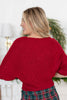 A woman shown from the back wearing a knit short sleeve red sweater and a green plaid skirt.