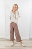 A woman modeling a cream pointelle-knit cardigan and brown wide-leg pants with white polka dots, paired with cream slip-on shoes, standing in a bright room with a white wall and light wood floor.