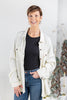 A woman wearing a cream ribbed waffle knit button-up long sleeve top over a black top and blue jeans.