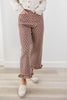 A woman wearing brown wide-leg pants with a white polka dot pattern and ruffled hems, styled with a cream knit cardigan and cream loafers on a light wood floor.