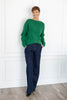 A woman stands wearing a bright green knit sweater and dark navy pinstriped trousers.
