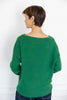 A woman is shown from the back wearing a green knit sweater with a wide boat neckline and dark blue pinstriped pants.